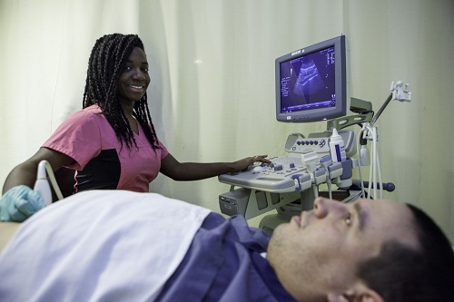 Smiling female student practices ultrasound scanning on male patient