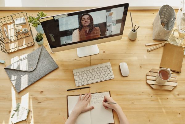 An unknown person on a video call at a desk taking notes