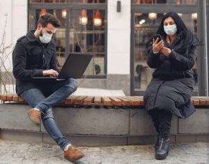 Two students in masks looking at their laptop and phone outside