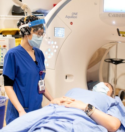 MRI Technologist standing over lying down patient in front of MRI machine
