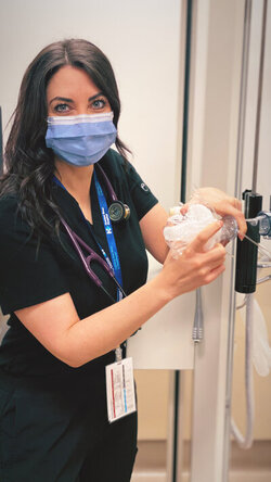 Kaitlyn Evers with mask on standing next to Respiratory Therapy equipment