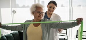 Physical therapist helping senior woman doing exercises with resistance band at home