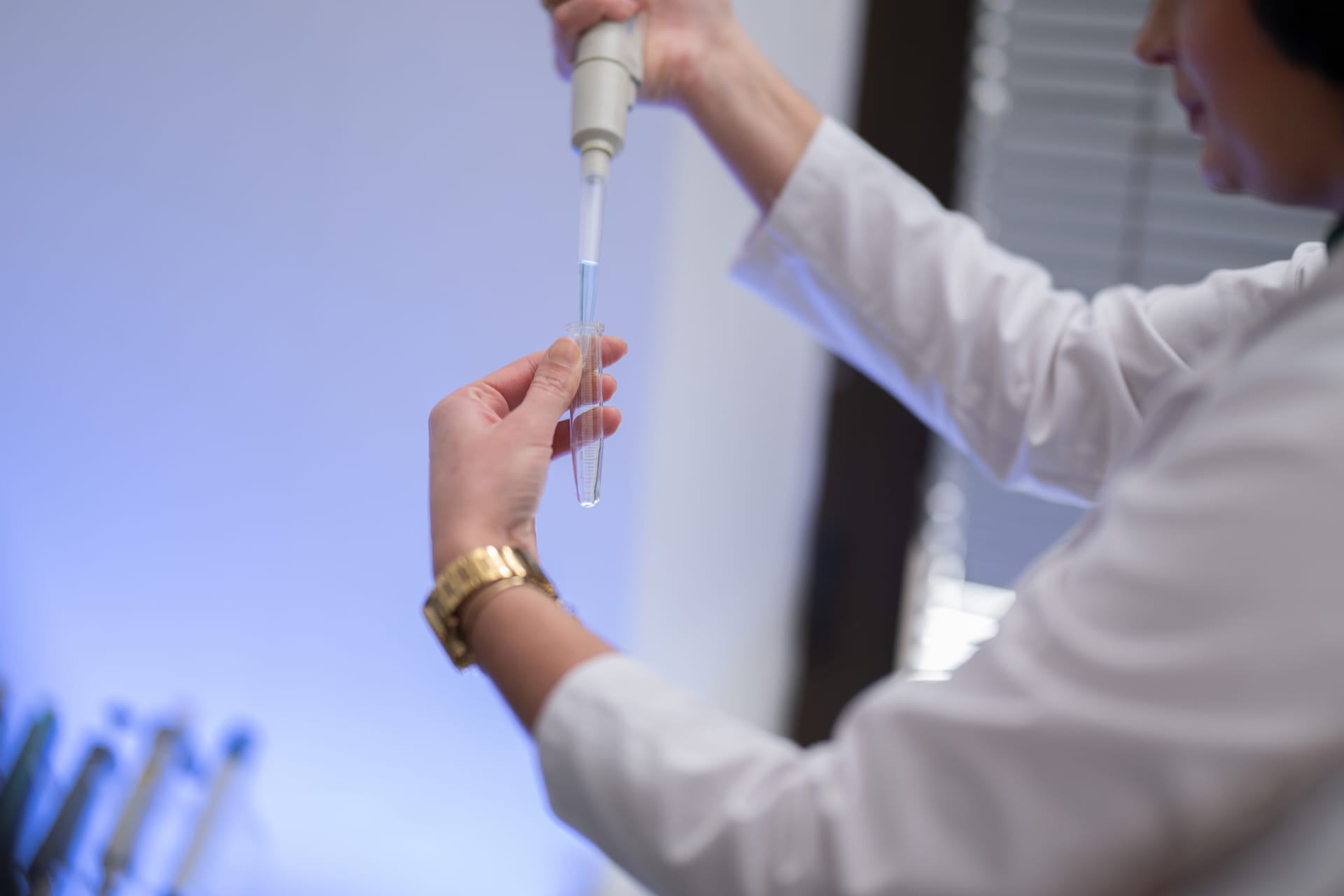 A person in a lab coat uses a pipette to transfer liquid into a test tube in a laboratory setting.