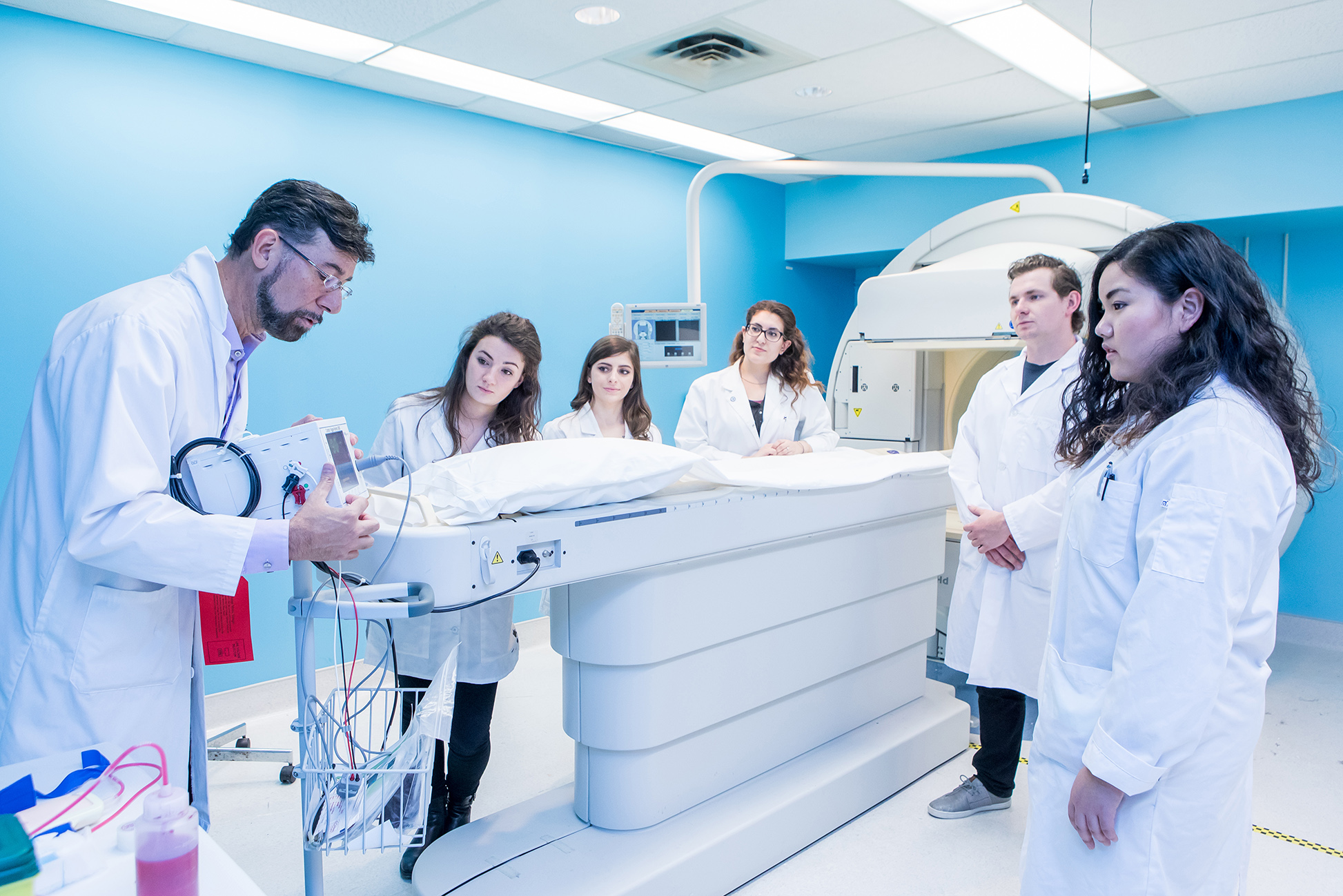 A doctor explains medical equipment to a group of students in a bright, modern clinical setting.