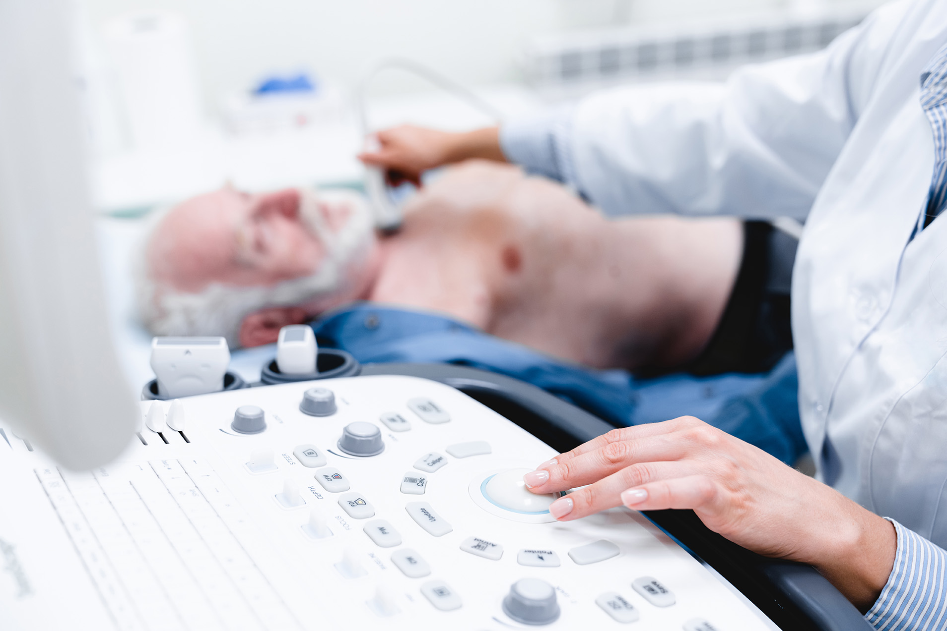 A doctor performs an ultrasound exam on an elderly man's chest using a medical ultrasound machine.
