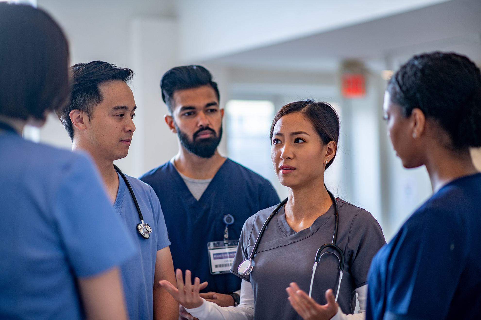 A group of healthcare professionals in scrubs having a discussion in a hospital hallway.