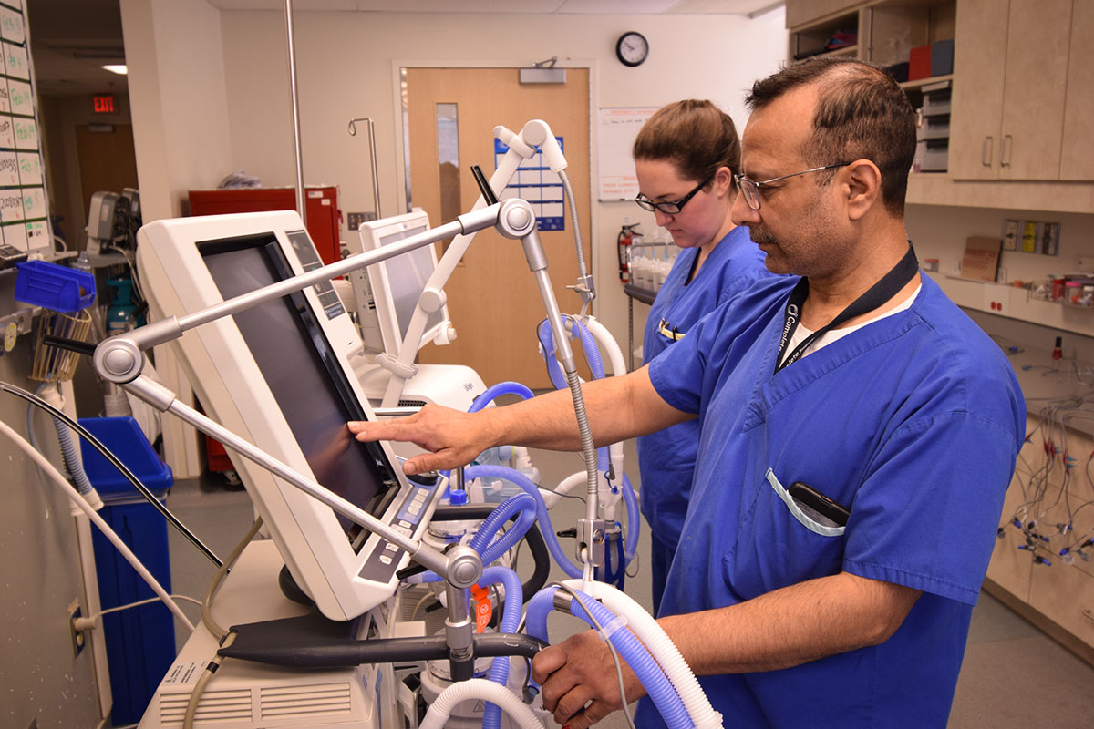 Two healthcare professionals in scrubs operate a touchscreen medical device in a hospital setting.
