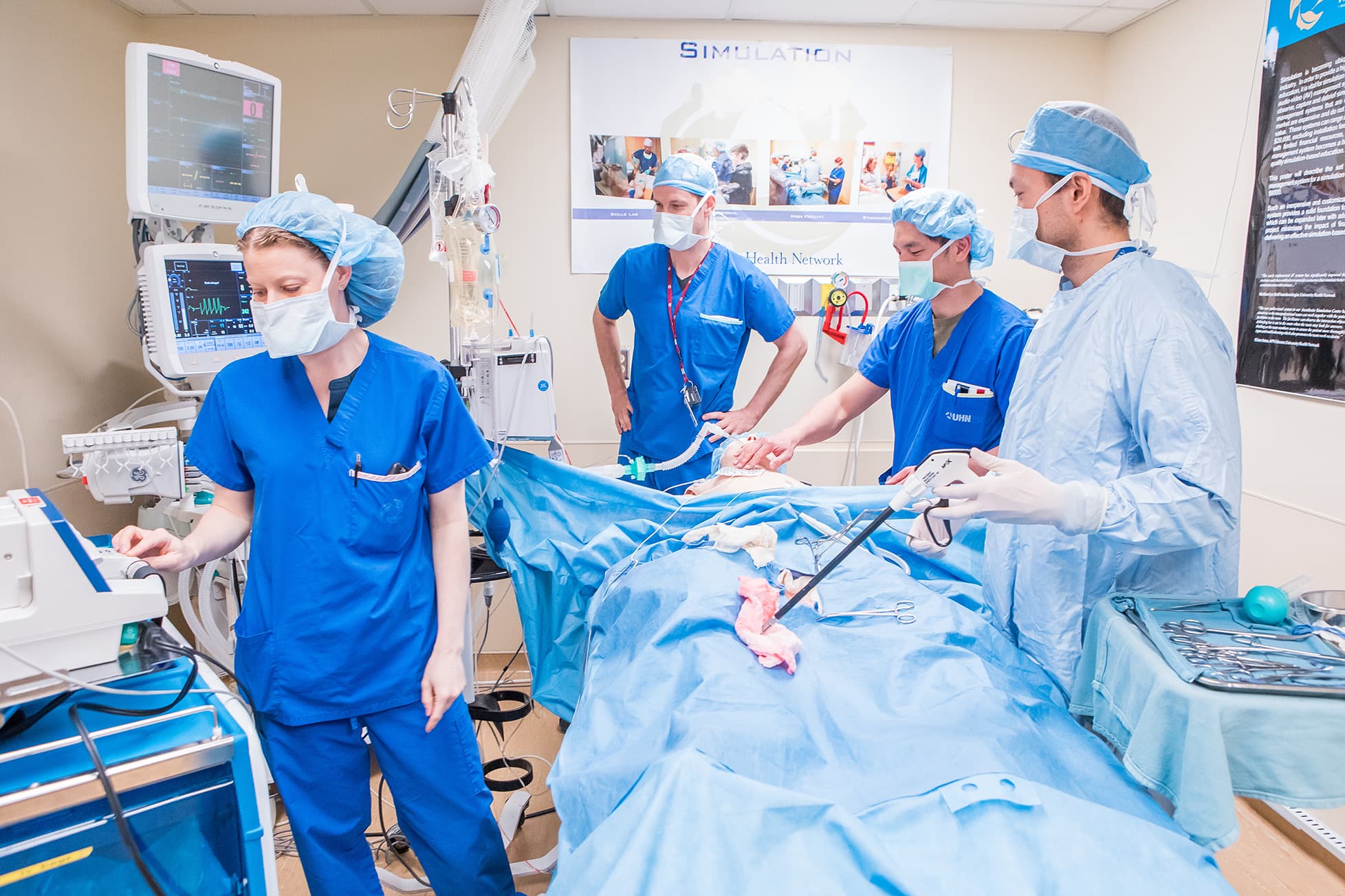 Four medical professionals in scrubs and masks perform a surgery simulation in a hospital training room.