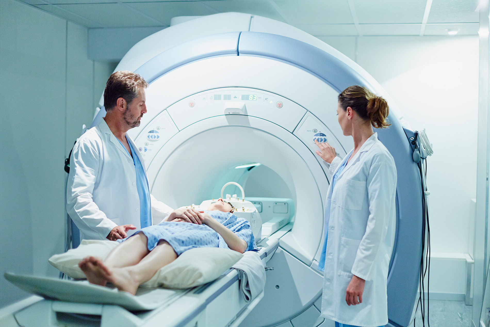 Two medical professionals operate an MRI machine as a patient lies on the table, preparing for a scan.