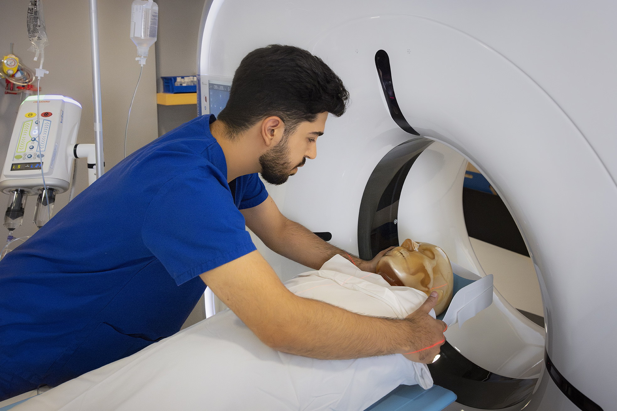 A healthcare worker positions a patient simulator inside a CT scanner in a medical facility.