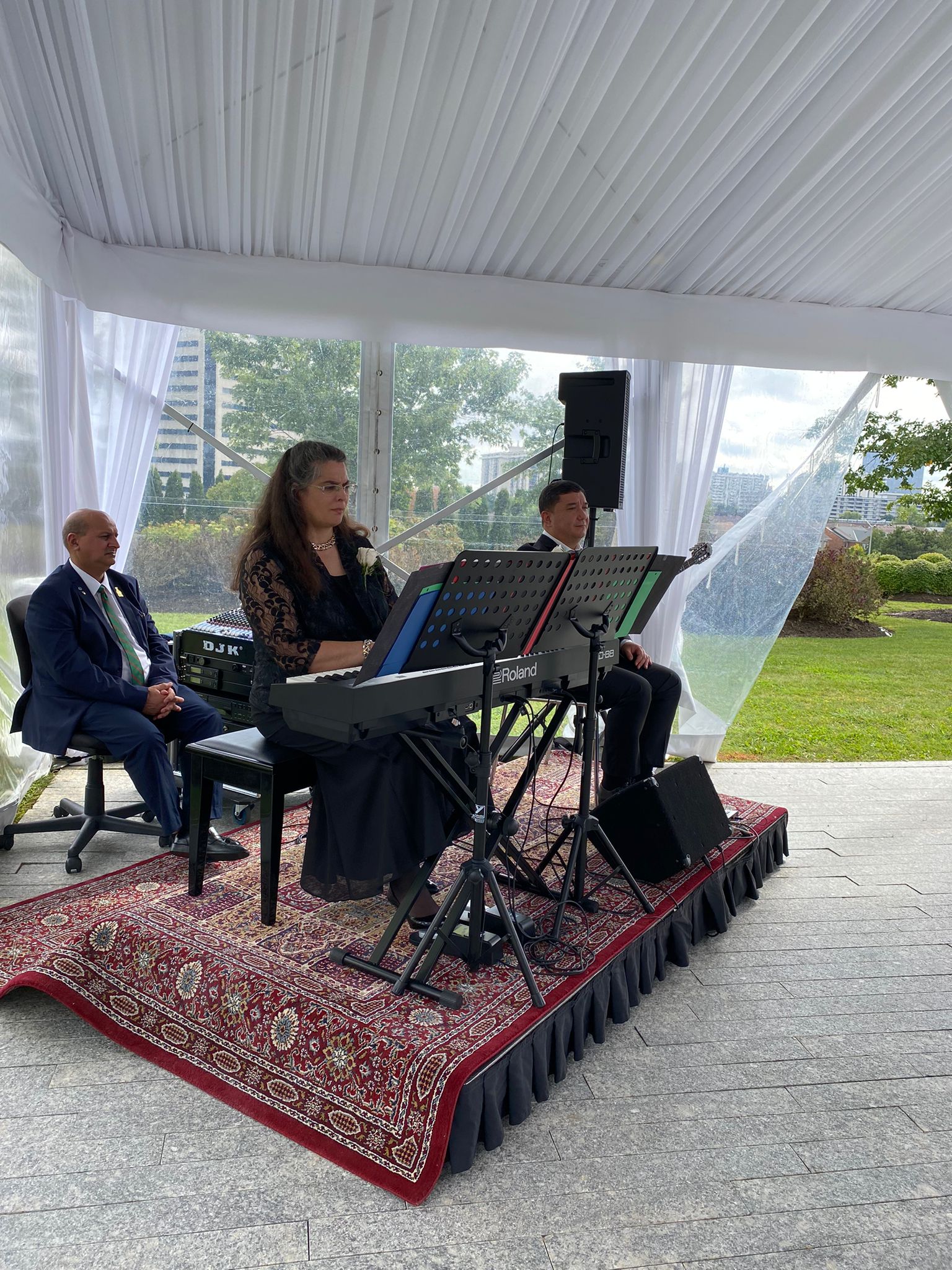 Catherine Ladhani performs at a piano at an outdoor ceremony, accompanied by a fellow musician.